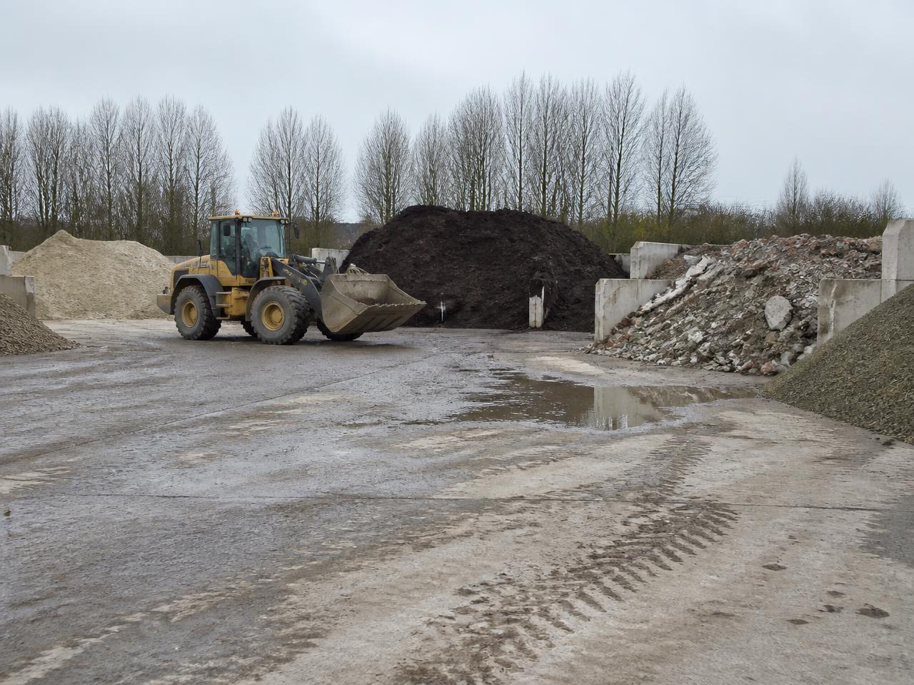Shovel op een gronddepot met gescheiden hopen zand, grond en granulaat