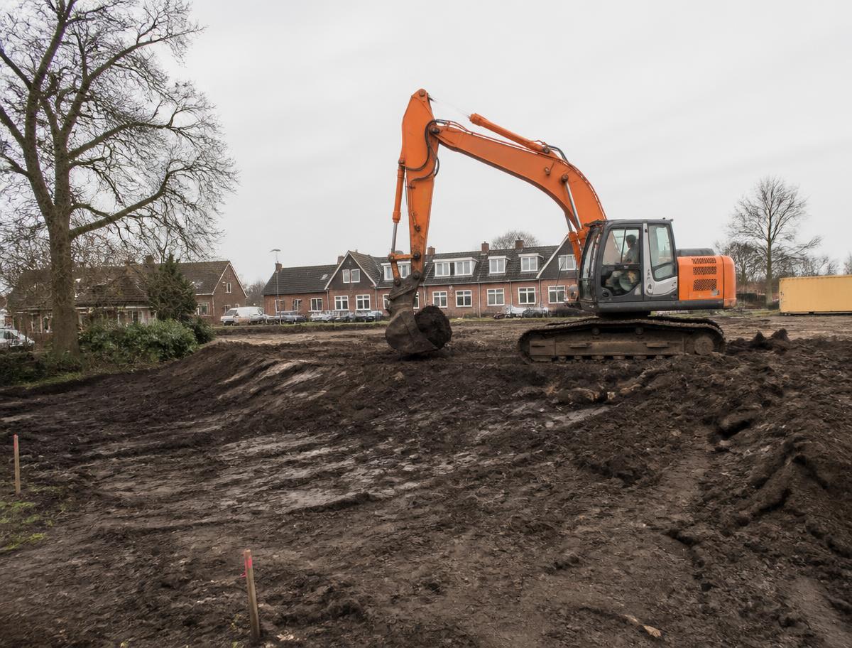 Graafmachine graaft grond af op een bouwterrein in een Nederlandse woonwijk